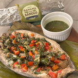 A prepared dish of Banana Leaf Bangus, which is a steamed fish filet with vegetables on top, served with a side of sweet lime and Thai basil sauce, presented on a banana leaf with a packet of banana leaf and a bowl of sauce in the background.