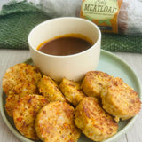 A plate of pork meatloaf slices next to a bowl of BBQ sauce, with a package of ranch seasoning visible in the background.