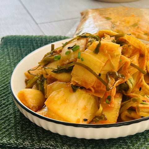 A bowl of Okinawa Kimchi, consisting of pickled vegetables, served on a white plate with a green mat underneath.