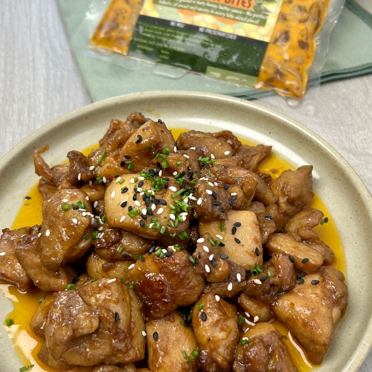 Stewed chicken dish with black and white sesame seeds on a beige plate, with a package in the background.
