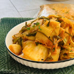A bowl of Okinawa Kimchi, consisting of pickled vegetables, served on a white plate with a green mat underneath.