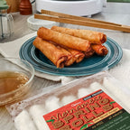 A plate of Vietnamese spring rolls with pork and veggies, accompanied by spiced vinegar in a bowl, with chopsticks on the side.